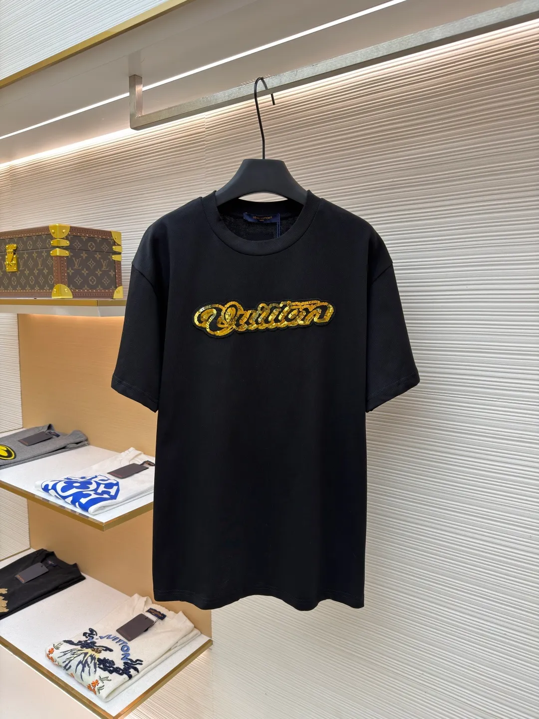 LOUIS VUITTON cotton round neck embroidered Vuitton signature logo short sleeves ●Original version: purchased and developed for 12300 ●Item number: 1682273-A10 ●Fabric: cotton fabric ●Technology: embroidery production ●Color: black ●Version: fitted version ●Weight: about 295 grams ●Size: S-M-L-XL ●Description: This white short-sleeved T-shirt is made of high-count combed cotton fabric and has been treated with pre-washing technology. It has a soft and skin-friendly touch and is not easy to deform. The silhouette of the shirt is a loose shoulder design, which meets the needs of modern casual wear. The core decoration area on the chest uses hand-beading and bronzing technology, and uses metallic gold sequins and embroidery threads intertwined to outline a three-dimensional letter pattern. The sequins are layered and inlaid, and each one is manually positioned and fixed by craftsmen to ensure a regular texture and uniform gloss. The edges of the letters are sewn with matte silk thread to form a visual contrast between gold and matte, while reinforcing the decorative structure to avoid falling off during wear. The neckline uses double-needle hemming technology and is matched with ribbed cuffs of the same fabric. It is durable and fits the neck. The overall craftsmanship combines handicraftsmanship with modern clothing technology, and the details show exquisite texture. The overall wiring is straight and delicate, the fabric is comfortable and soft, and the color is consistent without color difference. It can be matched with the same style to create a fashionable look and control various occasions. Customized accessories, complete with three standards, same style for men and women!